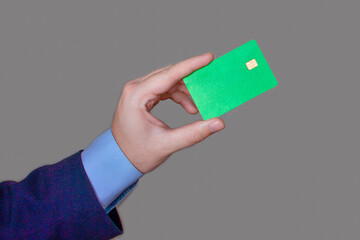 The hand of a man in a business suit holds a blank plastic card on a gray background.