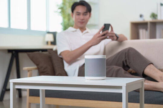 Technology and Lifestyle. Young man enjoying smartphone while smart speaker enhances home experience. - Powered by Adobe