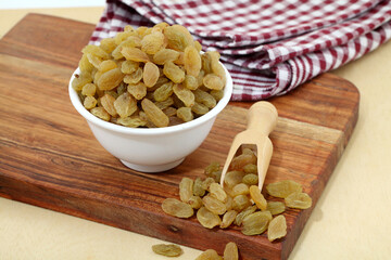 Close up of raisins in white ceramic bowl and wooden scoop