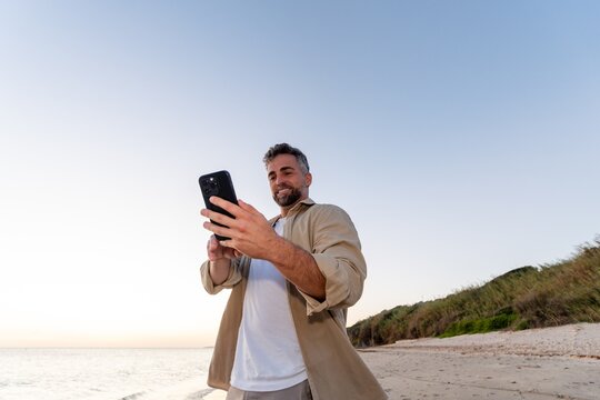 Man looking at smartphone on beach with clear sky
