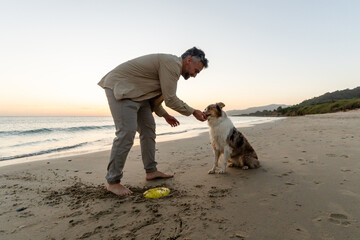 Man rewarding dog after playtime on beach