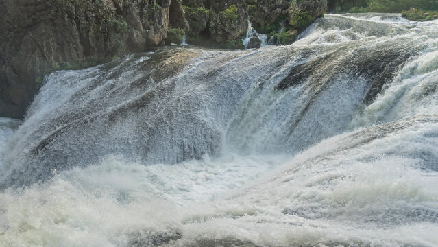A stormy mountain river. A fragment of the riverbed. Turbulent streams of white water foam on boulders. Splashes. Green vegetation on the coastal cliffs. China. Silver Chain Waterfall.   Guizhou  - Powered by Adobe