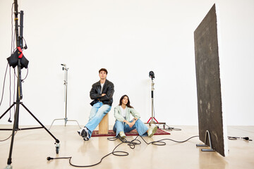 Models sitting during a studio shoot with lighting equipment nea