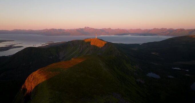 Telecommunication antenna lit up by sunset atop Storheia mountain ridge, aerial