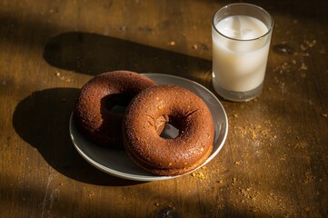 Two Chocolate Donuts on Plate with Glass of Milk, Warm Light, Rustic Table.