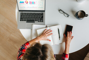 Overhead of woman multitasking with planner, phone and charts