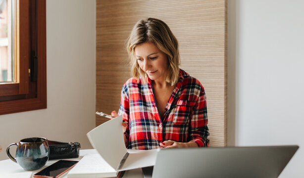 Mature woman reading notes next to laptop