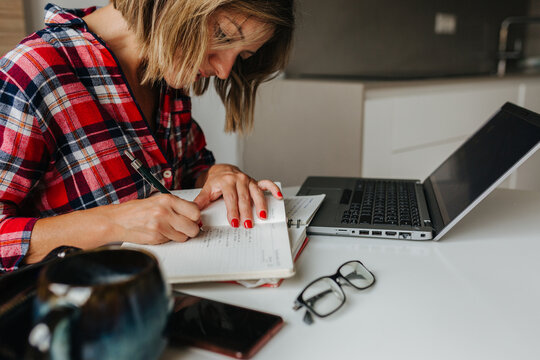 Portrait of woman writing with laptop and glasses on desk