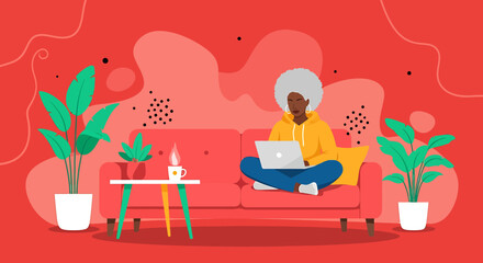 Woman working on a laptop on a couch surrounded by plants in a stylish apartment