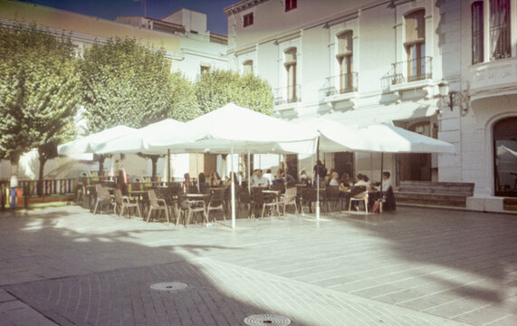 Film image of sunny square with umbrellas and people sitting outdoors