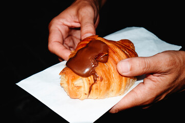 man holding a croissant topped with creamy chocolate