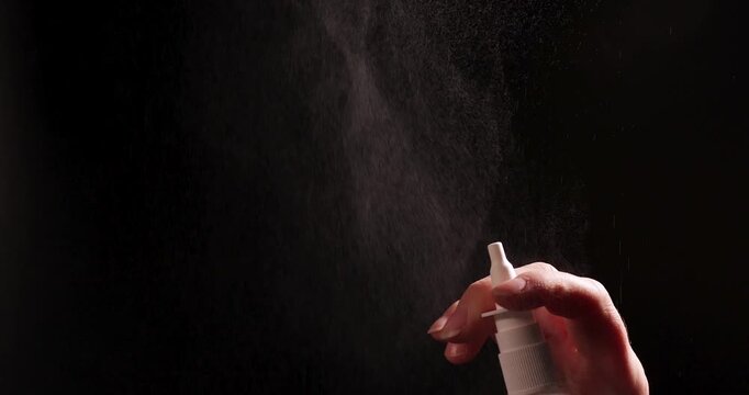 A hand is shown spraying a nasal spray bottle against a black backdrop. This illustrates the application and potential overuse associated with such medication.
