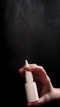 A hand holds a nasal spray bottle against a dark background. The nasal spray is then activated, spraying a mist, illustrating nasal congestion relief and issues of overuse.