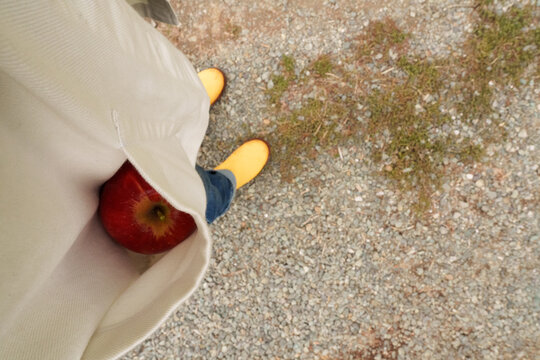 Bright Yellow Boots With Red Apple Resting in Pocket on Gravel Path