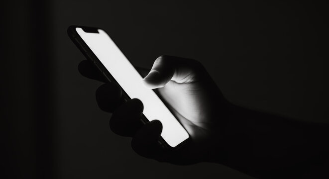 A silhouette of a hand interacts with a glowing screen, the stark contrast between light and shadow highlights the digital connection in modern communication. 
