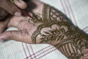 A traditional indian bengali woman's hand is getting decorated with mehendi as an art and ritual of bengali wedding