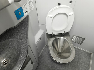 Public restroom in a commuter train car. A metal toilet, white walls, and a gray sink