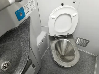 Public restroom in a commuter train car. A metal toilet, white walls, and a gray sink © Anton Belo