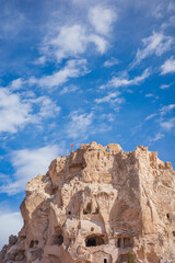 Fototapeta premium A striking view of the iconic Uchisar Castle in Cappadocia, Turkey, showcasing its massive natural rock formation carved with ancient cave dwellings. Perched at the top is a Turkish flag waving