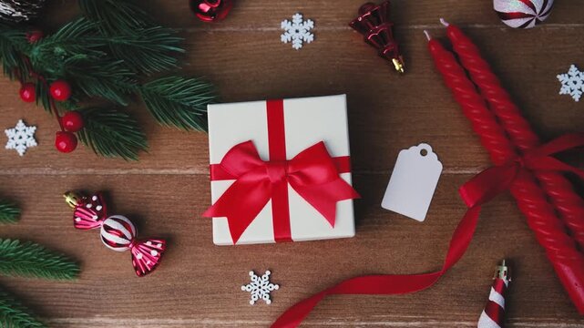 Christmas gift preparation with red ribbon, pine branches, candles and ornaments on wood