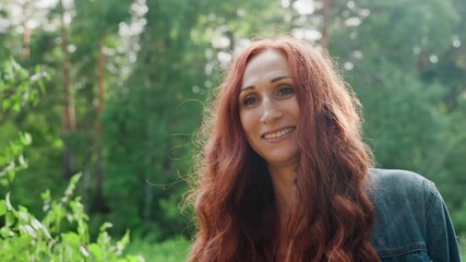 Portrait of family woman smiling gently in natural green forest, sunlight highlighting her face, peaceful outdoor atmosphere reflecting warmth, and maternal joy in bright summer day