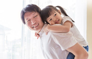 Portrait of smile father giving his young daughter a piggyback ride indoors, Warm and joyful family bonding moment at home. Father’s day