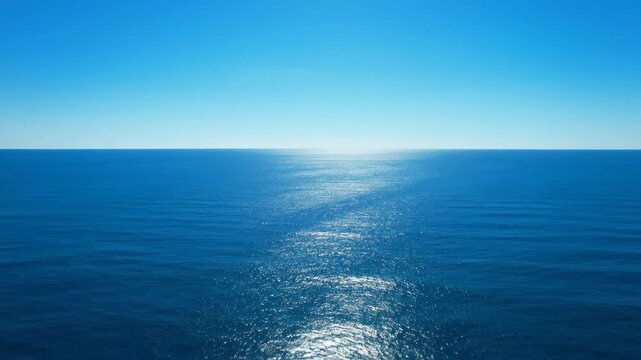 Sweeping drone shot moving slowly across the immense, blank horizon where deep blue ocean water meets a cloudless sky sweeping drone shot, open, coastline