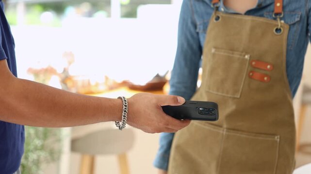 Courier and female small business entrepreneur verifying package via mobile device inside coffee shop, representing modern cashless payment, delivery service reliability, collaboration online orders