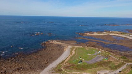 Guernsey. Backwards high drone footage of rugged coastline calm waves in crystal clear sea coming ashore in sandy bay at Grandes Rocque on sunny day with views to the horizon and rocky outcrops