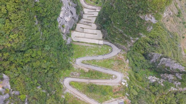 Flyover of the steep, sheer rock formations and the zigzag road carved into the cliffside at Lingpaishi, Wuxi County, China. Captures remote natural beauty and engineering. UHD.