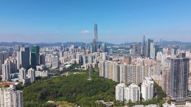 Aerial view of Shenzhen&rsquo;s skyline featuring Ping An Finance Centre rising above dense urban districts. Modern high-rises, green park areas, and distant mountains under a clear blue sky. China, UHD.