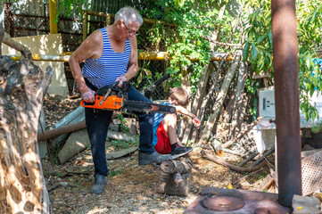 Grandfather teaching grandson how to cut wood with a chainsaw outdoors