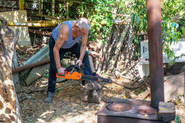 Grandfather teaching grandson how to cut wood with a chainsaw outdoors