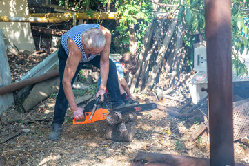 Grandfather teaching grandson how to cut wood with a chainsaw outdoors