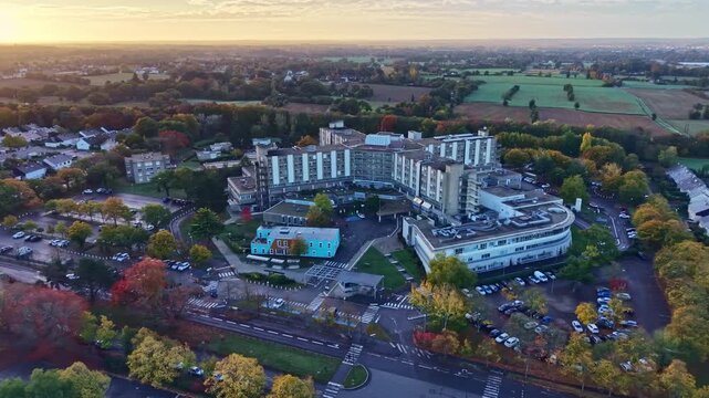 Morning light reveals large hospital complex with surrounding buildings and soft haze over the city, CHU Rennes. Aerial drone establish