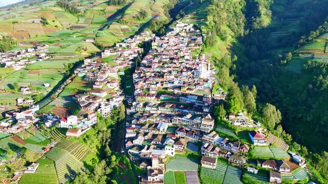 Aerial drone footage of a mountain village surrounded by terraced farms and lush green hills in the highlands of Indonesia. Nepal Van Java, Indonesia.
