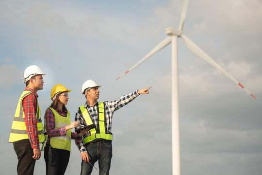Renewable energy maintenance. Engineer using digital tablet checking system of wind turbine at windmill field farm station. Wind turbine energy storage system. Workers meeting to check around the area