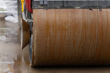 Close-up view of a heavy construction steamroller drum with wet rust patterns on the metal surface during roadwork operations on a rainy workday at an industrial jobsite