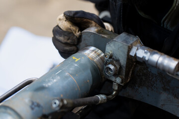 Worker performing detailed maintenance on hydraulic cylinder component, handling metal coupling and fittings with protective gloves during mechanical repair in industrial equipment environment