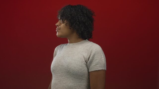 Woman in sweater looking sideways in studio with intense gaze and relaxed posture; contemplation focus.