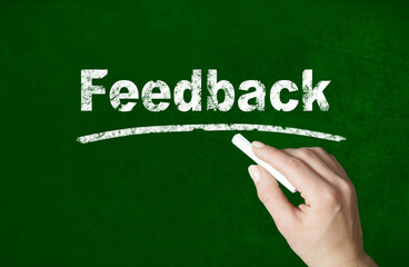 Person writing a Feedback word with chalk on a classroom style blackboard
