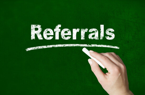 Person writing a Referrals word with chalk on a classroom style blackboard