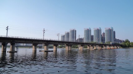 Elevated Railway Bridge Over River with Modern City Skyline - Powered by Adobe