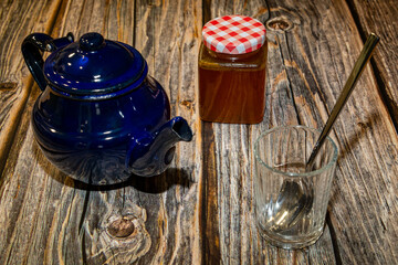 High angle of tea pot with lid and jar with honey placed on wooden table along with empty glass with spoon in daylight
