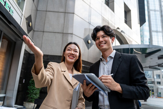 Asian young businessman and woman partner working outdoors in city. 