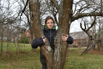 Young woman hugging a tree trunk in an autumn orchard