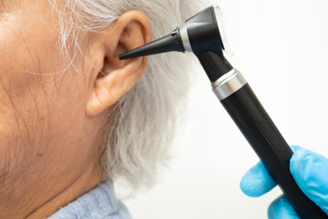 Otolaryngologist or ENT physician doctor examining senior patient ear with otoscope, hearing loss problem.