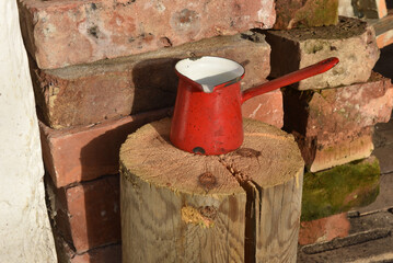 Red enamel cezve on a wooden log with bricks