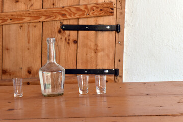 Clear glass bottle and shot glasses against wooden vintage furniture