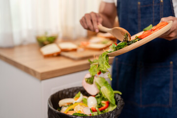 Close up of man throwing away fresh food scraps into trash bin. 